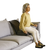 Woman sitting on a gray sofa with a back support device, wearing a yellow sweater and white pants.